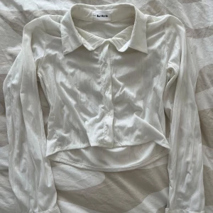 Vit croppad skjorta från Keken - Köpt i korea!🇰🇷Säljer en stilren vit croppad skjorta från Keren med klassisk krage och knäppning framtill. Skjortan har långa ärmar och är tillverkad i ett lätt, glansigt material som ger en fräsch look.