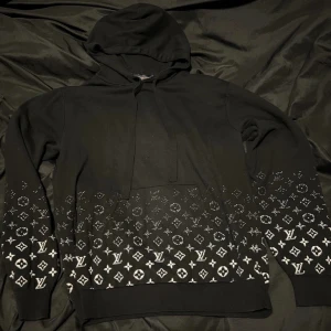 Svart hoodie från Louis Vuitton | byte - Säljer en svart hoodie från Louis Vuitton med klassiskt vitt LV-monogram och mönster nertill på både fram- och baksida. | ev byte