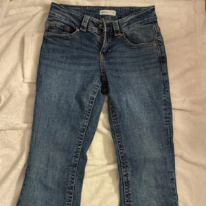 Blå bootcut jeans från Perfect Jeans - Säljer ett par klassiska blå bootcut jeans från Perfect Jeans. Jeansen har snygga fickdetaljer med lock och knappar bak, samt normal passform och utsvängda ben. Perfekta till sneakers eller boots.