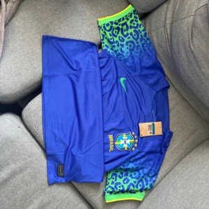 Blå Brasilien fotbollströja från Nike - Säljer en blå Brasilien fotbollströja från Nike med broderat CBF-märke och gula detaljer. Ärmarna har ett unikt blått och grönt mönster med neongula muddar. Perfekt för dig som vill sticka ut på planen eller heja på landslaget.
