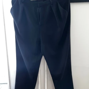 Svarta kostymbyxor från Gina Tricot - Snygga svarta kostymbyxor från Gina Tricot med klassisk passform. Byxorna har dragkedja och hake i midjan samt raka ben. Perfekta för en stilren look och passar till många olika outfits.