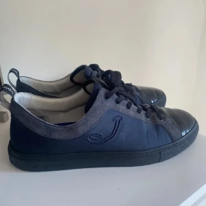 Mörkblå sneakers från Jacob Cohën - Snygga mörkblå sneakers från Jacob Cohën med svarta detaljer och snörning. Skorna har en rund tå, platt sula och är tillverkade i en kombination av skinn och syntetmaterial. Perfekta för dig som gillar stilrena och klassiska sneakers.