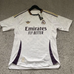 Real Madrid fotbollströja  - Säljer en vit Real Madrid fotbollströja med Mbappé och nummer 9 på ryggen. Tröjan har lila och guld detaljer, Adidas-logga och klubbmärke broderat på bröstet samt sponsortryck framtill. Kortärmad modell i lätt och ventilerande material.