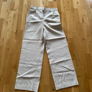 Beige vida byxor - Säljer ett par beige byxor med vida ben och hög midja. Byxorna har resår baktill i midjan och stängs med dragkedja och knapp framtill. Perfekta för en avslappnad och stilren look.