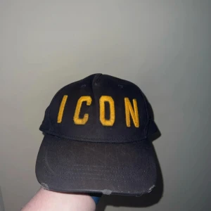 Dsquared2 keps  - Säljer en svart keps från Dsquared2 med broderad gul text 'ICON' framtill och 'DSQUARED2' baktill. Justerbar rem baktill för perfekt passform. Klassisk och stilren keps som sticker ut med sin tydliga logga.völdigt anvönd gör och tvätta 