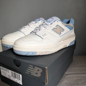 New Balance 550 - Säljer ett par fräscha New Balance 550 ”White University Blue” sneakers i vitt med ljusblå och grå detaljer. Perfekta för dig som gillar stilrena och sportiga sneakers med retrovibbar. Passar även dig som har storlek 41 EU. Köp innan 01/07 för 650kr och levererar direkt!!!