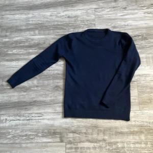 Mörkblå stickad tröja - En enkel och stilren mörkblå stickad tröja med rund halsringning och långa ärmar. Perfekt att bära till jeans eller över en skjorta för en clean look.