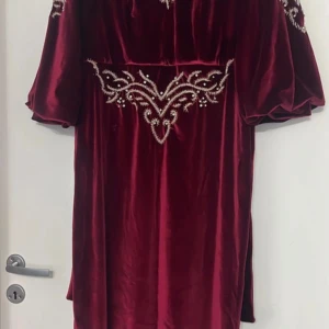 Vinröd sammetsklänning med pärldetaljer - Säljer en vinröd sammetsklänning med vackra pärldetaljer framtill och på axlarna. Klänningen har puffiga trekvartsärmar och en lös passform. Perfekt för dig som vill sticka ut med en elegant och lyxig look. Köpt för 500 kr denna året.