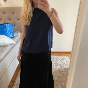 Mörkblå ärmlös blus med knyt i nacken - Säljer en stilren mörkblå ärmlös blus med rund halsringning och dekorativt knytband i nacken. Blusen har en rak passform och är tillverkad i ett mjukt, lätt material som passar perfekt till sommaren.