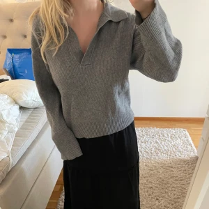 Grå stickad tröja med krage från BikBok - Säljer en grå stickad tröja från BikBok med krage och v-ringning. Tröjan har lång ärm och är ribbad i materialet, vilket ger en snygg och avslappnad look. Perfekt att matcha med jeans eller kjol.