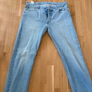 Ljusblå Levis 501 jeans - Klassiska ljusblå Levis 501 jeans med raka ben och knappgylf. Byxorna har fem fickor och är tillverkade i slitstarkt denim. Perfekta för dig som gillar en tidlös och avslappnad stil.