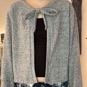 Grå kofta med knyt från Lager 157 - Mysig grå kofta från Lager 157 i storlek M med knytband framtill. Koftan är långärmad och har en enkel, rak passform. Perfekt att slänga över ett linne eller t-shirt för en chill look. Materialet känns mjukt och skönt mot huden. Använd ett fåtal gånger.