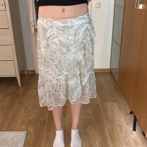 Vit mönstrad volangkjol Vero Moda XS - Superfin vit och ljusgrön långkjol från Vero Moda i storlek XS. Kjolen har ett tropiskt mönster, volang nertill och är gjord i ett lätt, luftigt material med resår i midjan. Perfekt för varma dagar när du vill ha en chill och fräsch look. Använd många gånger men i bra skick.