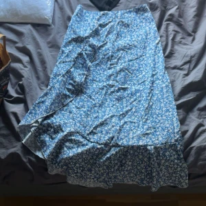 Blommig blå långkjol från SHEIN - Supersöt långkjol från SHEIN i blått med vitt blommönster. Kjolen har en lätt volang nertill och omlottkänsla i snittet. Perfekt för dig som gillar en flowy och feminin stil. Materialet är mjukt och lätt, perfekt för varmare dagar.