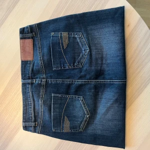 Mörkblå jeanskjol från grain de malice - Snygg mörkblå jeanskjol med klassiska fickor fram och bak, coola kontrastsömmar och knappdetalj i midjan. Rak modell som slutar ovanför knät. Tidlös denimstil som alltid funkar. Populär så var snabba!!