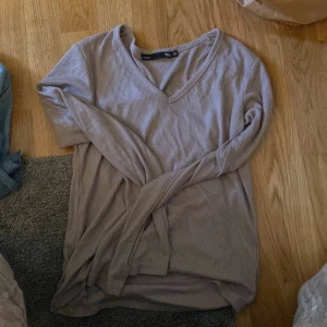 Ljusbeige ribbad tröja från 157 - Superskön ljusbeige långärmad tröja från 157 i ribbad bomull. Tröjan har v-ringning och en relaxed passform som är perfekt för chill dagar. Enkel att matcha med jeans eller kjol för en clean look.