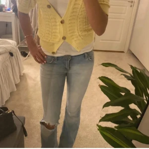 Ljusblå bootcut jeans - Säljer ett par ljusblå bootcut jeans med snygg slitning och hål på ena knät. Jeansen har klassisk femficksmodell, låg midja och är tillverkade i mjukt denimtyg. Perfekta för en avslappnad och trendig look.