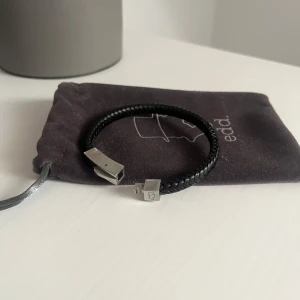 EDD Armband - Stilrent svart armband från edd. Med flätad design i läder och ett coolt magnetlås i silverfärgad metall. Perfekt accessoar för att lyfta din outfit med en modern touch. Levereras i originalpåse med logga. Originalpris=400kr
