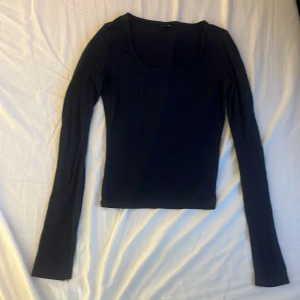 Svart långärmad topp från Gina Tricot - En mörkblå, figurnära långärmad topp från Gina Tricot i storlek XS. Toppen har en djup, rundad urringning och är tillverkad i ett mjukt och stretchigt material som sitter snyggt på kroppen. Perfekt att styla med jeans eller kjol. Nypris 199 kr.