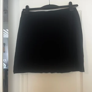 Svart kortkjol - Enkel och stilren svart kortkjol med rak passform. Kjolen är helsvart utan mönster eller detaljer. Använd fåtal gånger