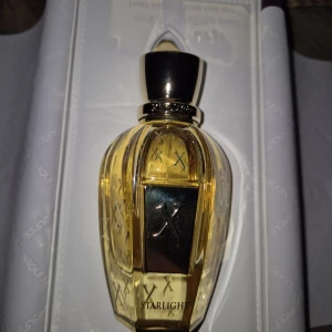 Xerjoff Starlight Parfym - Lyxig parfym från Xerjoff i modellen Starlight. Flaskan är elegant och guldig med detaljer i svart och guld, samt mönster av X över hela flaskan. Parfymen kommer i en exklusiv förpackning och har en sofistikerad, modern design.