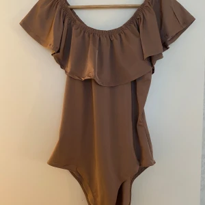 Brun body med volang - Snygg brun body med off-shoulder design och bred volang runt axlarna. Den är i storlek L men passar även M/S💗