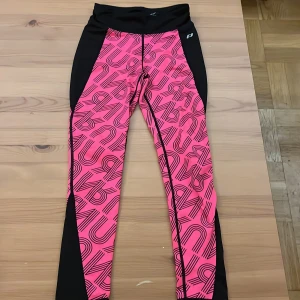 Rosa och svarta leggings Pro Touch - Snygga leggings från Pro Touch i rosa med svart grafiskt mönster och svarta paneler på sidorna. Hög midja med snörning för bästa passform. Perfekta för träning eller sportiga dagar. Materialet är stretchigt och följsamt för maximal rörelsefrihet.
