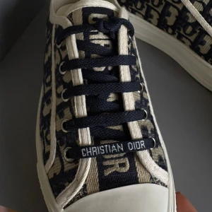 Christian Dior sneakers med monogram - Snygga sneakers från Christian Dior med ikoniskt blått och beige monogrammönster. Skorna har svarta snören med 'Christian Dior' tryckt framtill, vit gummisula och rund tå. Ovandelen är i textil och detaljerna ger en lyxig känsla till din outfit. Inget kvitto på eller box därav priset .