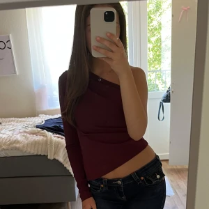 Vinröd oneshoulder topp - Säljer en vinröd oneshoulder topp med lång ärm på ena sidan och axelbandslös på andra. Snygg croppad passform som sitter tight och framhäver midjan. Perfekt för dig som vill sticka ut med en stilren och trendig look.