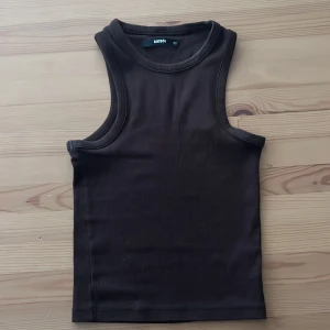 Brun ribbad linnetopp från BikBok - Säljer en brun ribbad linnetopp från BikBok i storlek XS. Toppen är ärmlös med klassisk rund halsringning och har en tight passform. Perfekt att styla med jeans eller kjol för en enkel och snygg look.