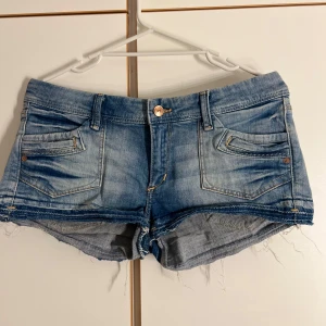 Blå jeansshorts - Snygga blå jeansshorts från &Shorts med låg midja och fransig, rå kant nertill. Klassisk femficksmodell med slitna detaljer och ljus tvätt. Perfekta för varma dagar och en avslappnad stil. Lappen för storleken finns inte kvar men kommer ihåg att det är storlek xxs