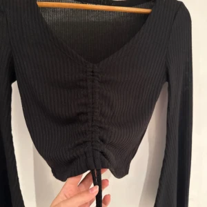 Svart croppad ribbad topp med snörning - Svart långärmad croppad topp från Shein med ribbad struktur och v-ringning. 