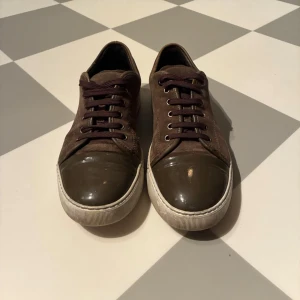 Bruna sneakers med mocka och lackad tå - Snygga bruna sneakers med ovandel i mocka och cool lackad tå i mörkbrunt. Skorna har mörkbruna snören och vit sula som ger en schysst kontrast. Perfekta för dig som gillar en stilren men ändå unik look.