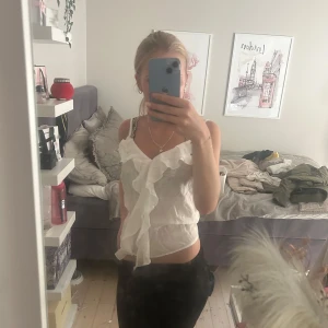 Vit volangtop från Kappahl XS - Helt ny Supersöt vit linnetopp från Kappahl i tunn och luftig viskosblandning. Toppen har smala axelband, v-ringning och en stor volang framtill som ger en romantisk vibe. Perfekt att styla med jeans eller kjol för en fräsch look. köpt för 300kr.