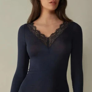 Svart långärmad topp med spets - Svart långärmad topp med djup v-ringning och snygga spetsdetaljer längs halsen. Tunn och mjuk känsla, perfekt för lager-på-lager. Sitter snyggt och har en feminin touch med spetsen framtill.