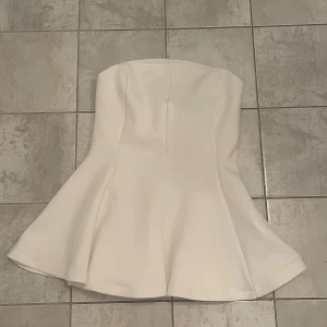Vit bandeau tubtopp med volang - Supersnygg vit tubtopp från Zara med utsvängd volang nertill. Toppen är axelbandslös och så snygg att styla med jeans eller någon fin kjol. Säljer då den tyvärr var för liten för mig, helt ny och oanvänd! 💞