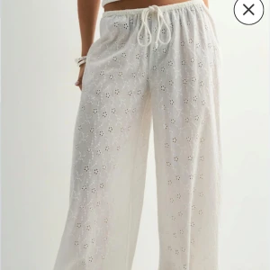 Vita broderade linnebyxor med snörning - Luftiga vita linnebyxor med broderade blommor och snörning i midjan. Byxorna har en relaxed fit och vida ben, perfekta för varma dagar. Snyggt hålmönster ger en somrig vibe och de är superbekväma att bära. Aldrig använda, prislapp kvar 