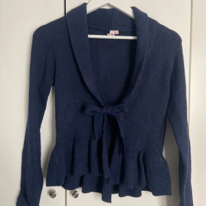 Mörkblå stickad kofta med volang - Supersöt mörkblå stickad kofta med volangkant och knyt framtill. Aldrig använd. Kontakta vid frågor osv 😊