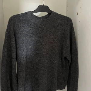 Mörkgrå stickad tröja från H&M - Mysig mörkgrå stickad tröja från H&M i enkel och klassisk modell. Tröjan har rund halsringning, långa ärmar och ribbade muddar. Perfekt för lager-på-lager och chill dagar. Passar dig som gillar basic och stilrent.
