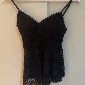 Svart spetsig linnetopp med volang - Supersnygg svart linnetopp med smala axelband och v-ringning. Bara andvänd när jag skulle prova den. Köpte den på en marknad så den har inget märke💞