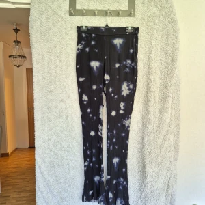 Svarta batikmönstrade vida byxor - Säljer ett par svarta byxor med vitt batikmönster och ribbad struktur. Byxorna har hög midja, vida ben och dragkedja i sidan. Materialet känns mjukt och stretchigt, perfekt för en chill och trendig look.