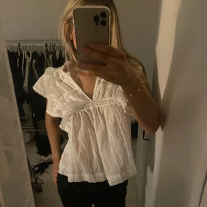Vit blus med volang och spetsdetaljer - Supersöt vit blus från Neo Noir med v-ringning, volangdetaljer på axlarna och fina spetsinslag. Blusen är ärmlös och har en luftig passform i tunt bomullstyg, perfekt för en fräsch och romantisk look. Storlek 34 motsvarar XS-S, inte använd många gånger. Nypris 600:-