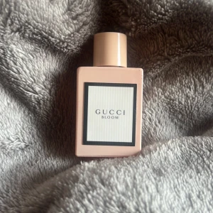 Gucci Bloom parfym  - Gucci Bloom parfym i en stilren, ljusrosa, rektangulär flaska med matchande lock. Flaskan har en minimalistisk etikett med svart ram och diskret text. Perfekt för dig som gillar exklusiva och blommiga dofter. Köpte den i ett sett för ungefär 1000kr men har jätt bort dom andra så bara den här kvar. Den är oanvänd har kanske använt den 1 gång.