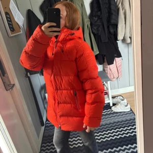 Röd pufferjacka med huva - Säljer en riktigt fet röd pufferjacka med huva och dragkedja framtill. Jackan är oversized och har två fickor med dragkedja på sidorna. Perfekt för kalla dagar när du vill sticka ut lite extra. Snygg och bekväm passform. Köpt för 3000kr