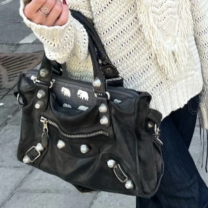 Balenciaga väska - Ikonisk svart handväska från Balenciaga. Har vissa defektes och insidan är sydd( bild 5) det finns små hål på tyget i insidan. Den är sydd vid vissa ställen och strådet vid handtaget är tillagt. Skriv för att få se fler bilder!💗🫶