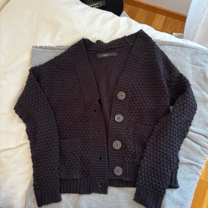 Svart stickad kofta från Vero Moda - Mysig svart stickad kofta från Vero Moda med grov struktur, stora knappar framtill och två fickor. Koftan har lång ärm och bred ribbad kant vid ärmslut och nederkant. Perfekt för lager-på-lager och chill höstkvällar.
