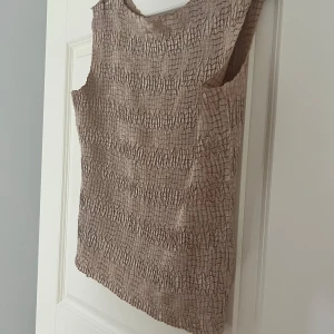 Beige linnetopp m struktur - Säljer en superfin satintopp med fint strukturmönster. Perfekt för S/M men har även funkat på mig som är XS/S i lösare passform.