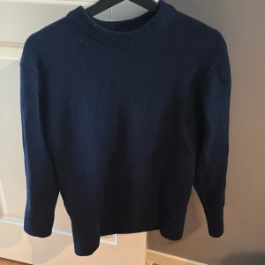 Mörkblå stickad tröja från H&M - En enkel och stilren mörkblå stickad tröja från H&M i regular fit. Tröjan har rund halsringning med ribbad kant och långa ärmar. Perfekt för lager-på-lager och passar till det mesta i garderoben.