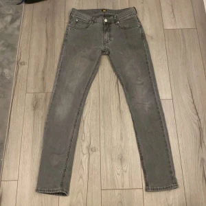 Gråa jeans Lee - Snygga grå jeansbyxor från Lee i modellen Luke. De har en klassisk femficksdesign och en dragkedja. Perfekta för en stilren look. Slim fit som nya.   Hör av dig vid funderingar!