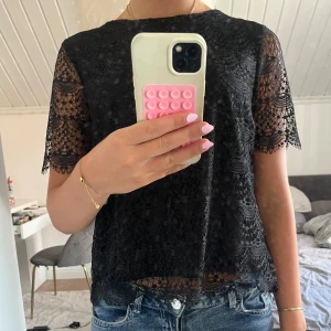 Svart spetsblus med kort ärm - Säljer en svart blus i spets med korta ärmar och rund hals. Blusen har ett detaljerat spetsmönster. Priset kan diskuteras vid snabb affär